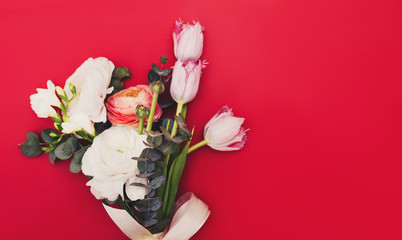 A small bouquet of flowers on red background. Tulip, eucalyptus branches, Ausin roses and ranunculus. Flat lay. Wedding concept. Copy space