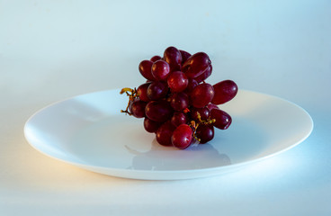 Red grapes  photographed in awhite plate against white background with space for content