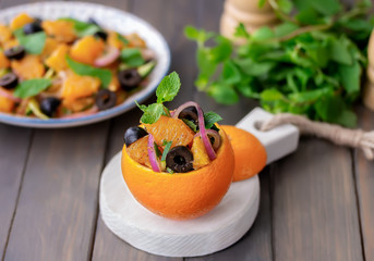 Raw orange salad with black olive, red onion and mint served in an orange. Wooden background, selective focus. © Iryna