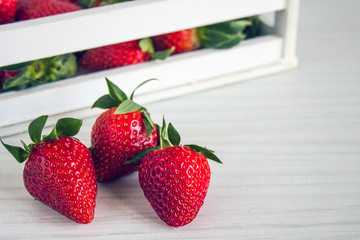 Bright ripe red strawberries in a white decorative box and on the table close up with copy space