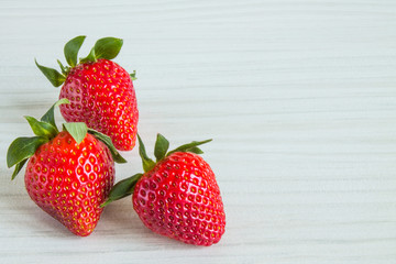 Three ripe red strawberry berries close up on a white wooden background with copy space