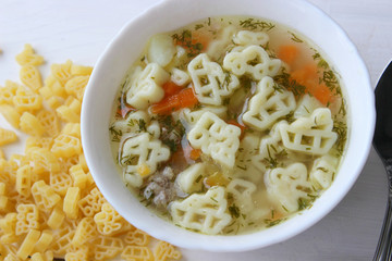 Hot soup, broth with meatballs, carrots, macaroni and fresh herbs.Delicious lunch on a wooden Board. Children's food, macaroni soup in the form of an airplane and a car.