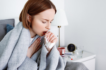 Sick woman suffering from pulmonary cough due to cold, flu, respiratory infections, pneumonia, bronchitis, covered in blanket at home in isolation at quarantine. Covid-19 coronavirus self treatment