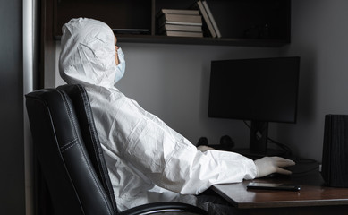 Man in medical mask and protective suit, rubber gloves sits at home and works with pc at the table during quarantine. Designer, artist, architect, businessman at remote work in a pandemic covid.