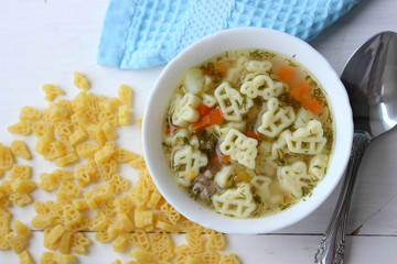 Hot soup, broth with meatballs, carrots, macaroni and fresh herbs.Delicious lunch on a wooden Board. Children's food, macaroni soup in the form of an airplane and a car.