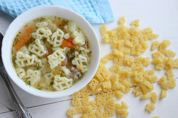 Hot soup, broth with meatballs, carrots, macaroni and fresh herbs.Delicious lunch on a wooden Board. Children's food, macaroni soup in the form of an airplane and a car.