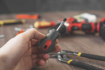 Man's hand holds a small screwdriver among a pile of other tools