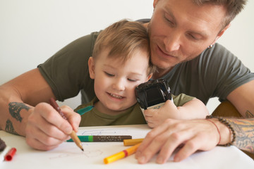 Young father helps son at age of two draw, teaches alphabet. A small boy is sitting on his dads lap...