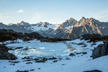 Frozen alpine lake and sunset on distant peaks in the Talkeetna Mountains in July.