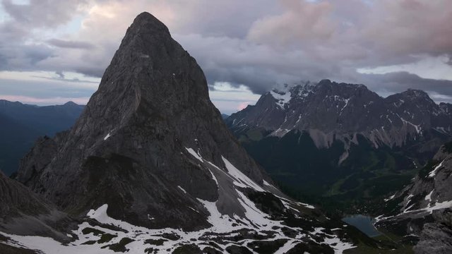 Time lapse of mountain peak Sonnenspitze and lake Seebensee in Ehrwald during sunset with dramatic moving clouds, snow fields, Zugspitze in the background, Tyrol Austria.