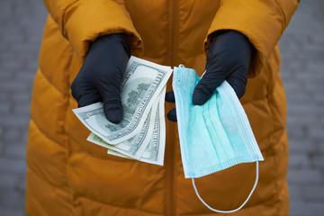 Hands holds 100 dollar bills for a surgical face mask signifying a spike in price of face mask...