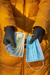 Hands holds 100 dollar bills for a surgical face mask signifying a spike in price of face mask...