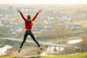 Fototapeta na wymiar Young woman jumping with outstretched arms and legs outdoors on a distant city background. Relaxing, freedom and wellness concept.