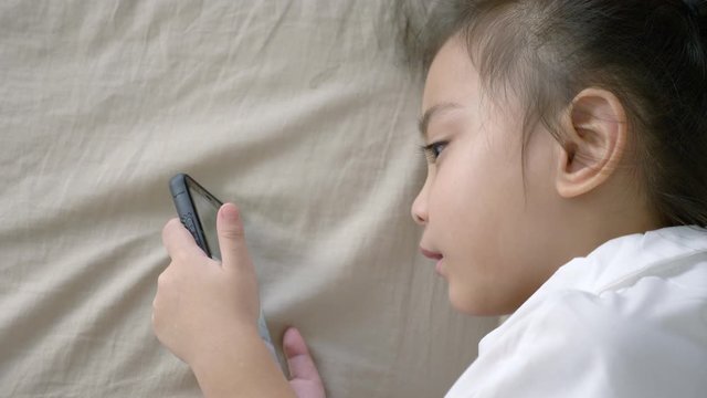 baby girl play mobile phone.young girl watching on smartphone and lying on bed at home