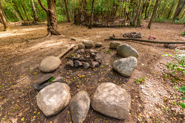  A campsite in the woods, with stone chairs and a fireplace green trees and a path through the forest.