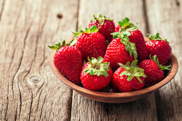 Freshly picked Strawberry in wooden bowl on wooden background. Healthy eating and nutrition.