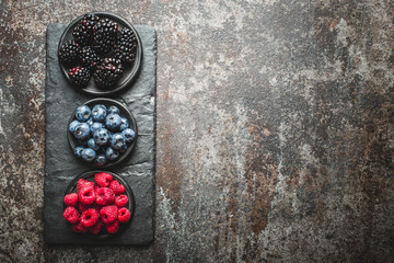 Fresh berries with raspberries, blueberries, blackberries in bowl on a stone stand on a dark metal background.