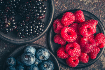 Fresh berries with raspberries, blueberries, blackberries in bowl on a dark metal background.