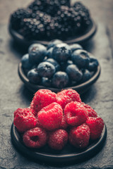 Fresh berries with raspberries, blueberries, blackberries in bowl on a stone stand on a dark metal background.