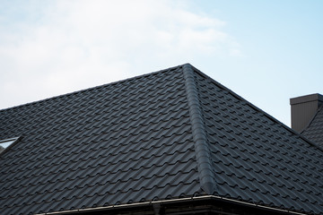 Fototapeta na wymiar Black metal tile roof. Roof metal sheets. Modern types of roofing materials. Roof of the house, metal roof tile against the blue sky. Building.