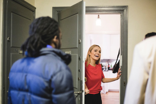Cheerful woman greeting friends while standing at doorway