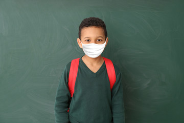 Cute African-American schoolboy wearing protective mask in classroom. Concept of epidemic