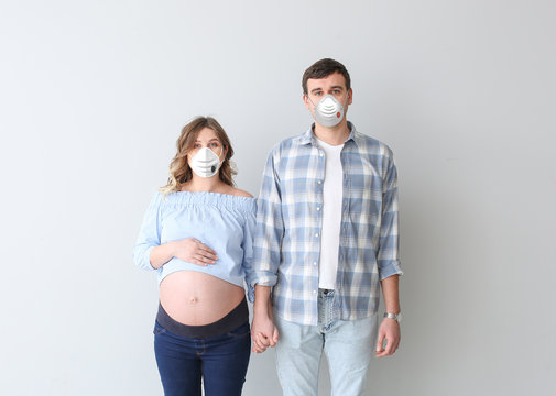 Young pregnant couple wearing protective masks on grey background. Concept of epidemic