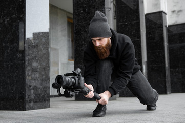 Bearded Professional videographer in black hoodie holding professional camera on 3-axis gimbal...
