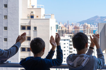 Fototapeta premium Family applauding medical staff from their balcony. People in Spain clapping gratitude on balconies and windows in support of health workers, doctors and nurses during the Coronavirus pandemic