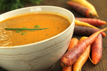 Carrot cream in a bowl with fresh vegetables on wooden table