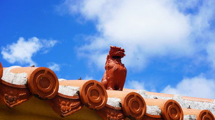 Sculpture of the mythical shisu on the roof. clay statuette on a Japanese tiled roof on background blue sky      