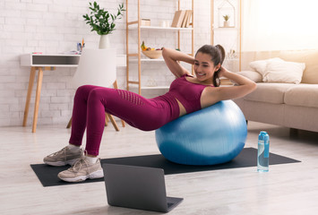 Stay home. Young girl doing exercises with fitness ball while watching online tutorials on laptop