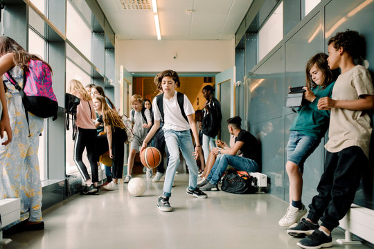 Boy playing with basketball during lunch break in school corridor