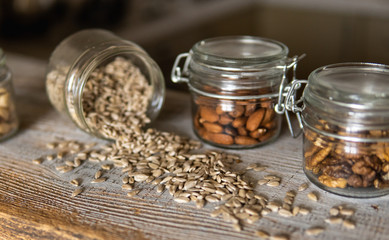 Sunflower seeds scattered on the white vintage table from a jar with other nuts on background. Healthy vegetarian protein nutritious food. Sunflower seed on rustic old wood.