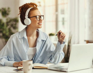 Young pleased woman in headphones using laptop at home.