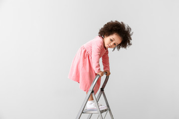 Little African-American girl playing with step ladder on light background. Child in danger © Pixel-Shot
