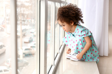 Fototapeta na wymiar Little African-American girl near window. Child in danger
