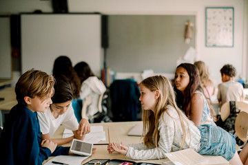Female student leaning over table while friends sitting in classroom