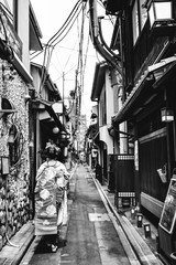 Beautiful geisha walking in kimono at traditional alley in Kyoto downtown, Japan (in black and white)