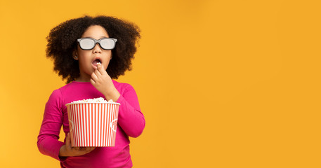 Kids cinema. Black little girl wearing 3D glasses and eating popcorn