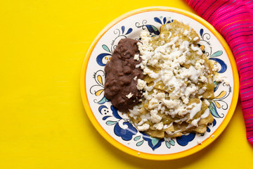 Mexican green chilaquiles with beans on yellow background