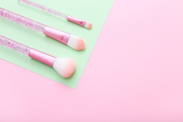 Set of makeup brushes on pink and green colored composed background.