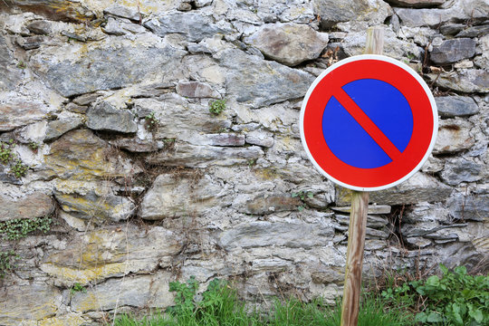 Panneau de signalisation routi&egrave;re devant un mur en pierre le long d'une route : interdiction de stationner.