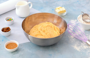 Bowl with sweet dough and products on color background