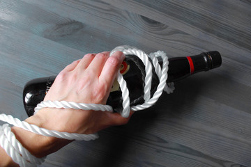 Imagen conceptual de una mano humana atada con cuerda a una botella de vino simbolizando la...