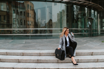 Fototapeta premium A young attractive businesswoman with a bag is sitting on the stairs in front of the company