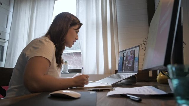 Young beautiful woman works at a laptop. Smiling girl teacher gives online lessons. Business videoconference. Office at home. Work in conditions of self-isolation.