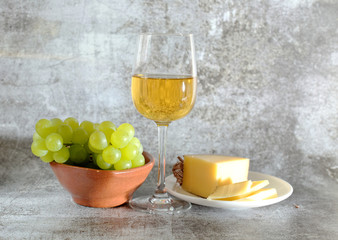 composition of a glass of white wine cheese and a bunch of grapes on a plate.
