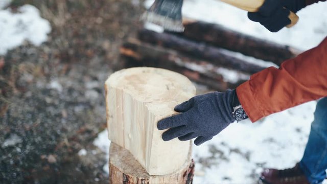 Men's hands in gray gloves and watches holding an axe and chopping wood in winter. Close up