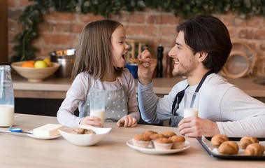 Healthy breakfast. Caring young dad feeding little daughter with homemade cookies